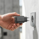 Une main tient le chargeur secteur noir devant une prise murale, ses deux broches rondes dirigées vers celle-ci. Les ports USB-C