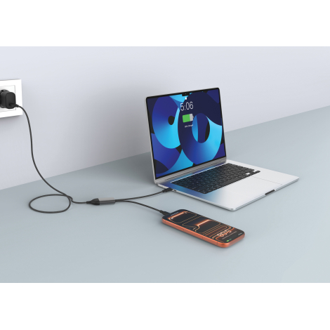 Câble de recharge Terra noir utilisé pour alimenter simultanément un ordinateur portable argenté et un smartphone posé sur un bu