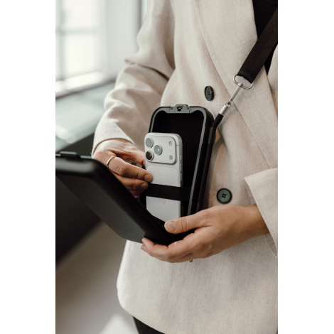 Femme plaçant un smartphone dans le compartiment intérieur de son étui de voyage porté en bandoulière, avec une bande élastique 