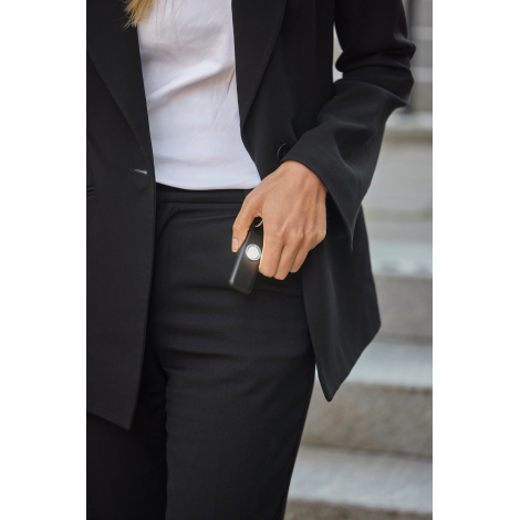 Une femme vêtue d'un tailleur noir et d'un haut blanc tient une alarme d'urgence noire dans sa main, avec la lampe circulaire al