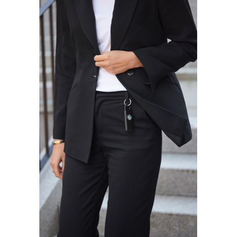 Une femme en tailleur noir soulève le pan de sa veste pour montrer une alarme d'urgence noire suspendue à un passant de son pant