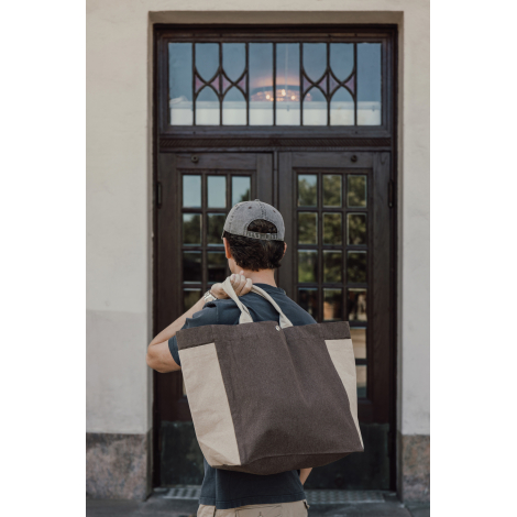 Homme portant un sac shopping marron et écru à l'épaule par ses poignées courtes, illustrant son volume généreux et sa forme sou