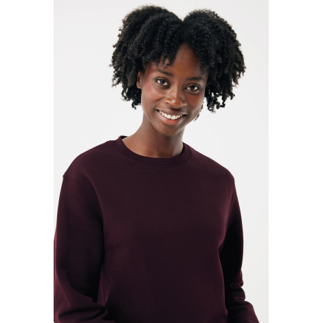 Portrait d'une femme souriante aux cheveux crépus, vêtue d'un sweat bordeaux uni à col rond et manches longues, photographiée de