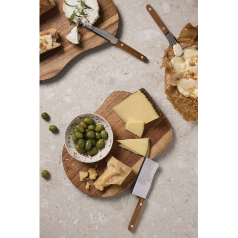 Deux plateaux en bois accueillent différents fromages, des olives et du pain sur une table en pierre claire. Les couteaux à from