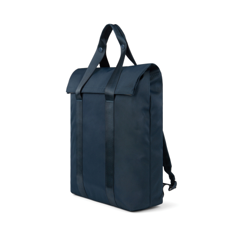 Sac à dos bleu marine vu de trois quarts, avec rabat supérieur replié, deux poignées en sangle réunies au sommet par des boutons