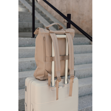 Sac à dos beige posé sur une valise rigide claire devant un escalier en pierre, maintenu par sa bande arrière autour de la poign