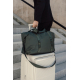 Sac de week-end vert foncé posé sur une valise rigide claire devant un escalier en pierre. Une personne vêtue de noir tient la p