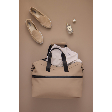 Sac de week-end extensible beige ouvert, contenant une chemise blanche, photographié de dessus sur un fond assorti. Deux mocassi