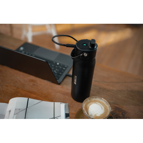 Gourde filtrante noire posée sur une table en bois à côté d'un ordinateur portable, d'un carnet ouvert et d'une tasse de café. U