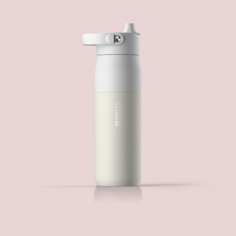 Gourde isotherme beige clair et gris clair présentée de face sur un fond rose pâle, avec embout de boisson apparent et poignée r