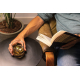 Homme assis dans un fauteuil en cuir marron, un livre ouvert à la main, tenant un verre de whisky ambré avec des glaçons métalli Homme assis dans un fauteuil en cuir marron, un livre ouvert à la main, tenant un verre de whisky ambré avec des glaçons métalli