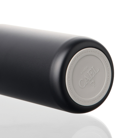 Gros plan sur le dessous d'une bouteille isotherme noire mate, montrant une base circulaire en silicone gris clair, ornée d'insc
