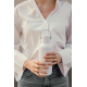 Vue rapprochée d'une femme en chemise blanche et jean gris, tenant à deux mains une bouteille isotherme blanche mate, avec un bo Vue rapprochée d'une femme en chemise blanche et jean gris, tenant à deux mains une bouteille isotherme blanche mate, avec un bo
