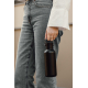 Gros plan sur une femme en jean gris et chemise blanche, portant une bouteille isotherme noire mate par son anse métallique arge Gros plan sur une femme en jean gris et chemise blanche, portant une bouteille isotherme noire mate par son anse métallique arge
