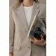 Femme vêtue d'un blazer beige et d'un haut blanc, tenant contre elle une bouteille isotherme noire mate avec manchon en silicone