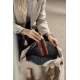 Femme blonde en blazer beige, plaçant une bouteille isotherme bordeaux mate dans un grand sac beige ouvert. La bouteille possède