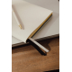 Gros plan sur un carnet beige à couverture texturée et tranches dorées, accompagné d'un stylo blanc à pointe dorée. Deux rubans Gros plan sur un carnet beige à couverture texturée et tranches dorées, accompagné d'un stylo blanc à pointe dorée. Deux rubans