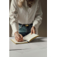 Femme en chemise blanche et jean bleu écrivant avec un stylo clair dans un carnet ouvert aux pages lignées et tranches dorées, p Femme en chemise blanche et jean bleu écrivant avec un stylo clair dans un carnet ouvert aux pages lignées et tranches dorées, p