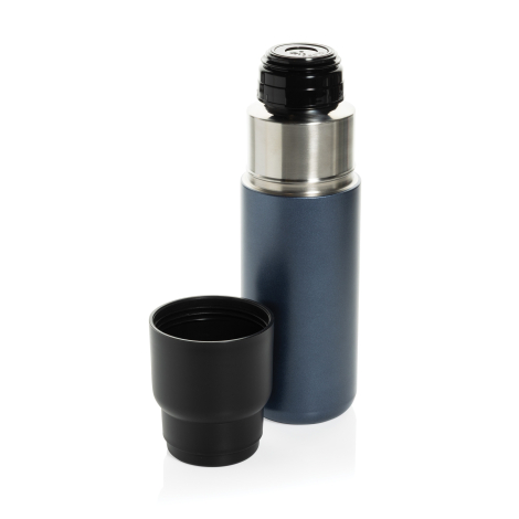 Bouteille isotherme bleu foncé ouverte, avec un col en métal argenté et un bouchon verseur noir. Sa tasse noire amovible est pos