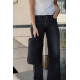 Une femme en t-shirt blanc et jean noir, cadrée du buste aux jambes, tient à la main un cube de rangement noir par sa boucle de 