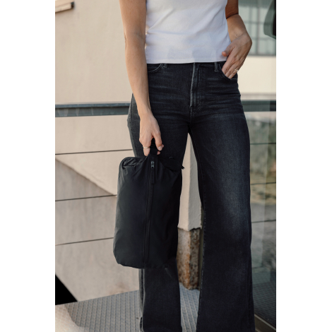 Une femme en t-shirt blanc et jean noir, cadrée du buste aux jambes, tient à la main un cube de rangement noir par sa boucle de 