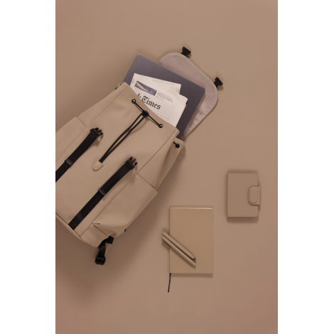 Sac à dos beige ouvert, vu du dessus, contenant un ordinateur portable et un journal. Son ouverture à cordon noir et son rabat r