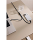 Câble multifonction bleu foncé reliant un ordinateur portable argenté à un smartphone blanc, posé sur une table beige. Un verre Câble multifonction bleu foncé reliant un ordinateur portable argenté à un smartphone blanc, posé sur une table beige. Un verre