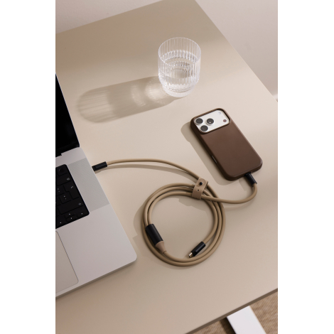 Câble de recharge beige partiellement enroulé sur une table, avec une attache assortie et un connecteur USB-C libre. Il relie un